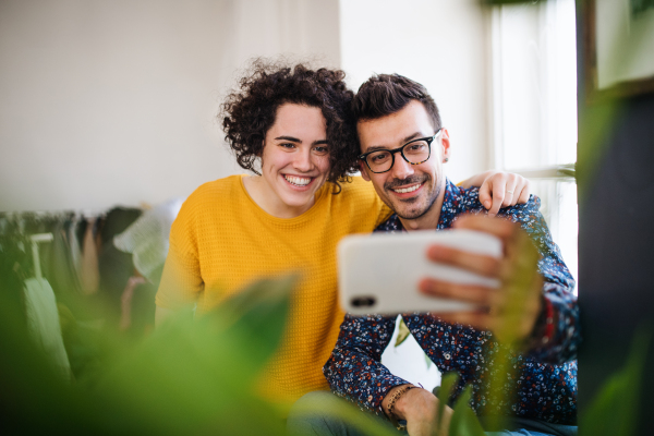 Two young cheerful friends with smartphone indoors, taking selfie. House sharing concept.