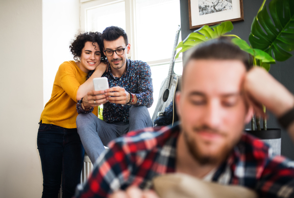 A group of young cheerful friends with smartphone sitting on sofa indoors, house sharing concept.