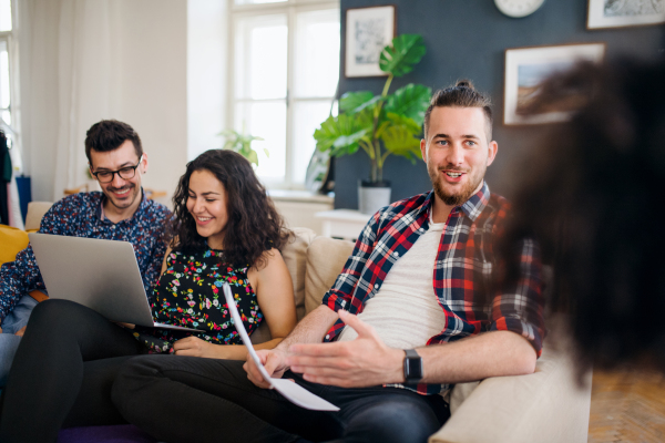 A group of young cheerful friends with laptop sitting at table indoors, house sharing concept.