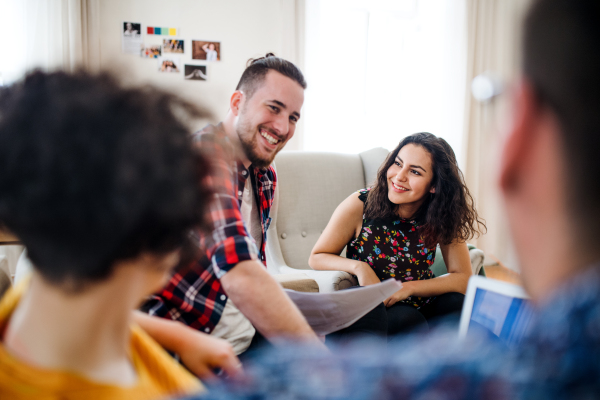 A group of young cheerful friends with laptop sitting at table indoors, house sharing concept.