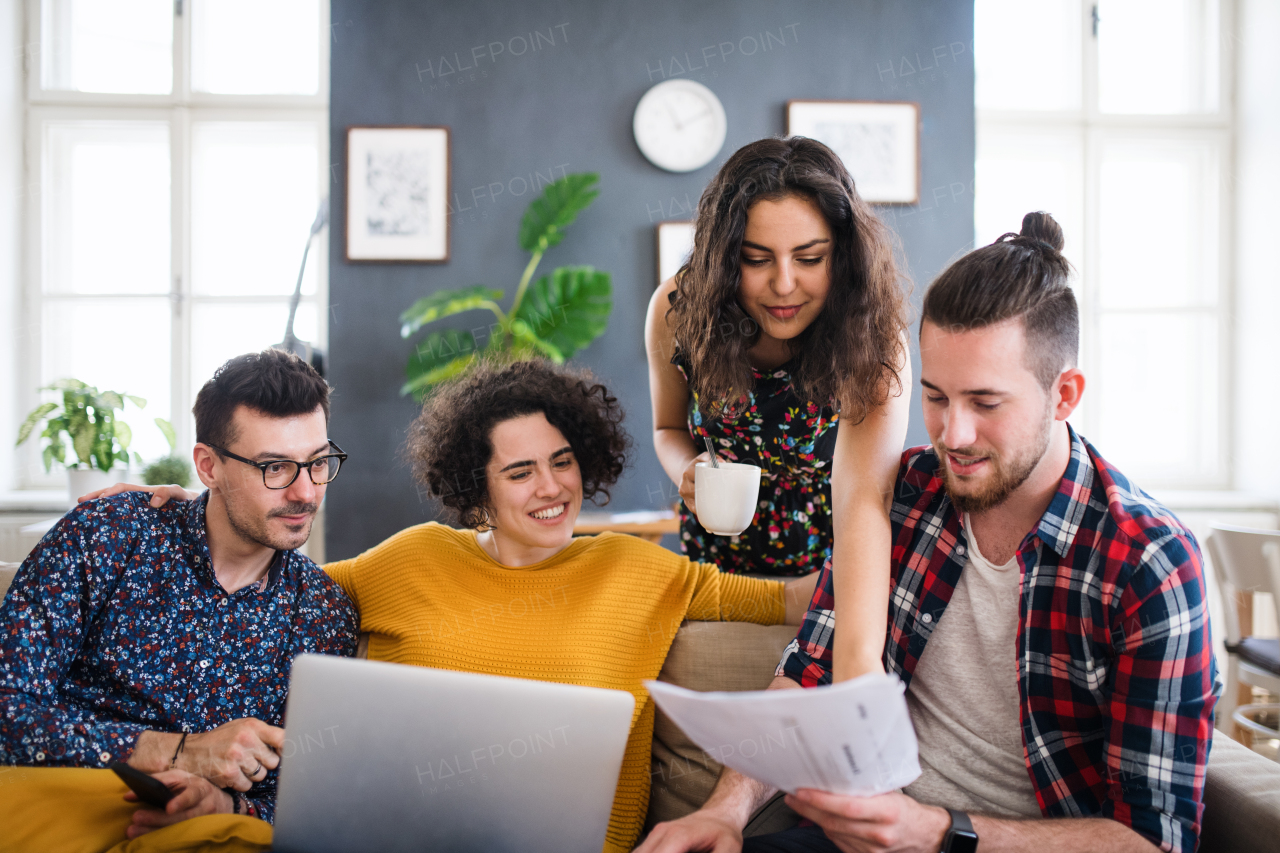 A group of young cheerful friends with laptop sitting at table indoors, house sharing concept.