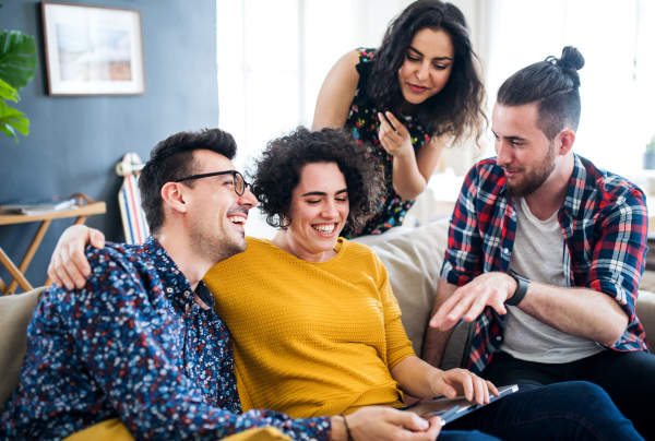 A group of young cheerful friends with tablet sitting indoors, house sharing concept.