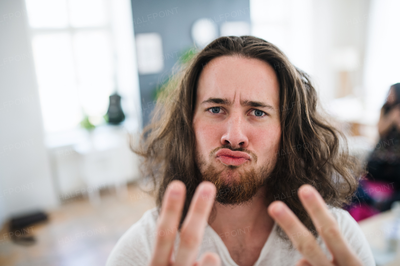 A portrait of young hipster man with long hair indoors, fingers forming V for victory.