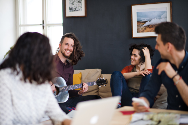 A group of young cheerful friends with guitar indoors at home, house sharing concept.