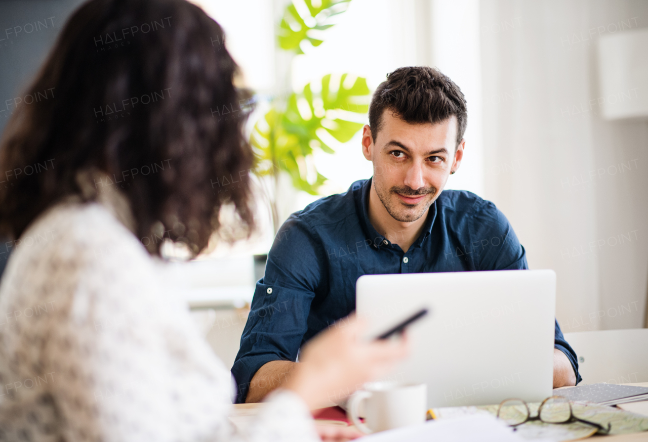 Two young cheerful friends with laptop sitting at table indoors, working. A house sharing concept.