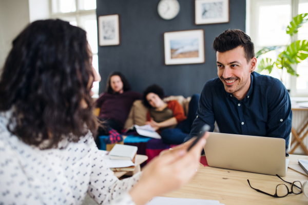 A group of young cheerful friends with laptop sitting at table indoors, house sharing concept.