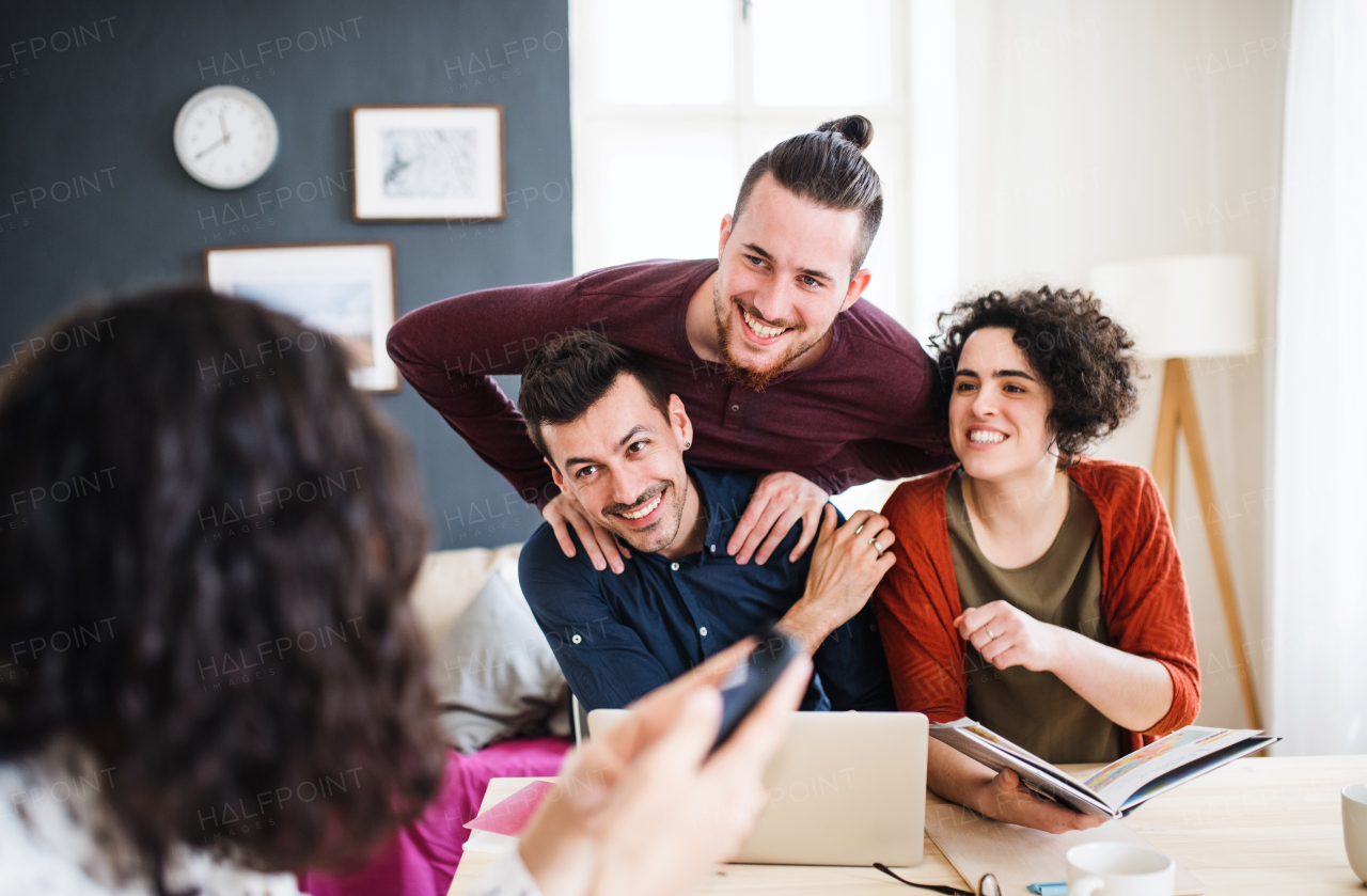 A group of young cheerful friends with laptop sitting at table indoors, house sharing concept.