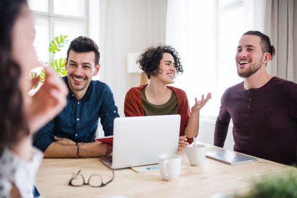 A group of young cheerful friends with laptop sitting at table indoors, house sharing concept.