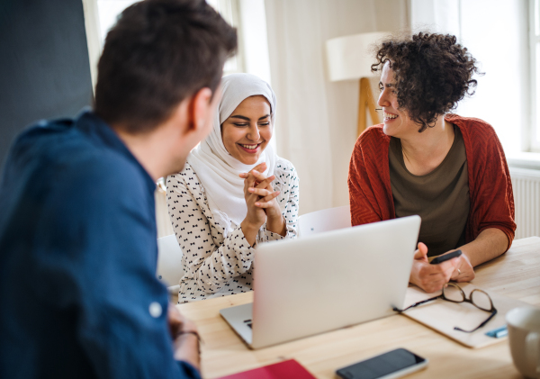 A multi-ethnic group of young cheerful friends with laptop sitting at table indoors, house sharing concept.