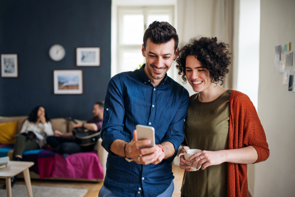 A group of young cheerful friends with smartphone indoors, house sharing concept.