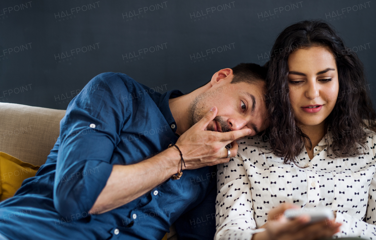 Young cheerful friends with smartphone sitting on sofa indoors, house sharing concept.