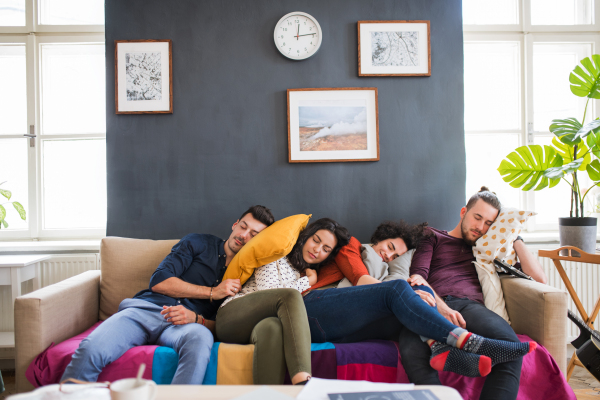 A group of young cheerful friends indoors at home, sleeping on sofa. House sharing concept.