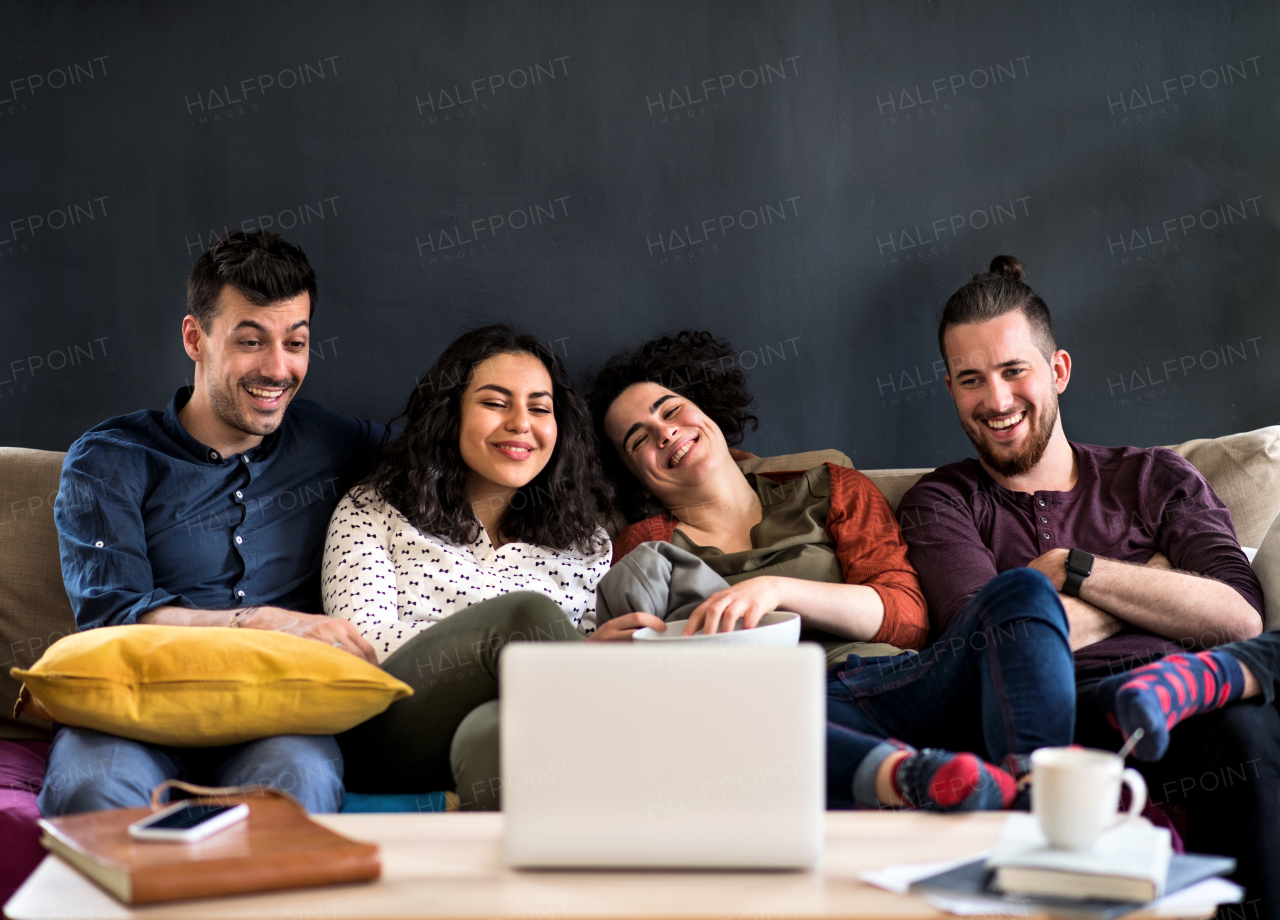 A group of young cheerful friends with smartphone sitting on sofa indoors, watching film. House sharing concept.