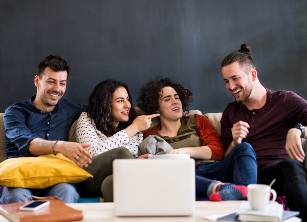 A group of young cheerful friends with smartphone sitting on sofa indoors, watching film. House sharing concept.