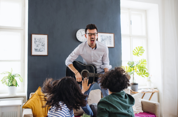 A group of young cheerful friends with guitar indoors at home, house sharing concept.