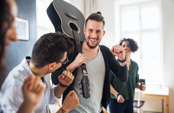 A group of young cheerful friends with guitar indoors at home, house sharing concept.