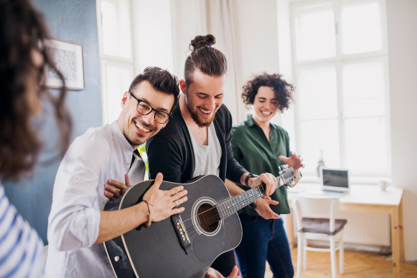 A group of young cheerful friends with guitar indoors at home, house sharing concept.