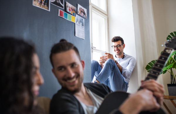 A group of young cheerful friends with smartphone indoors, house sharing concept.