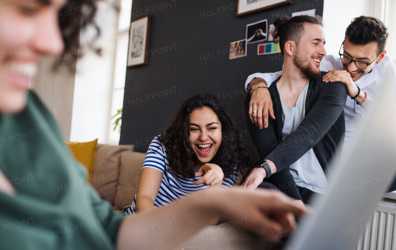 A group of young cheerful friends with laptop sitting at table indoors, house sharing concept.