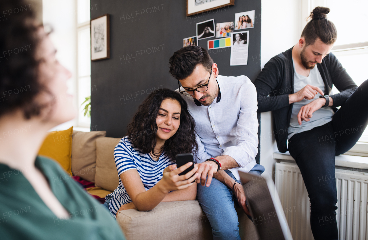 A group of young cheerful friends with smartphone sitting at table indoors, house sharing concept.