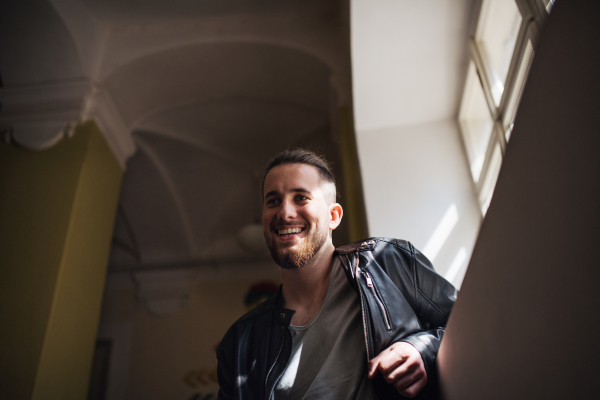 A low-angle portrait of young hipster man standing indoors in a corridor.