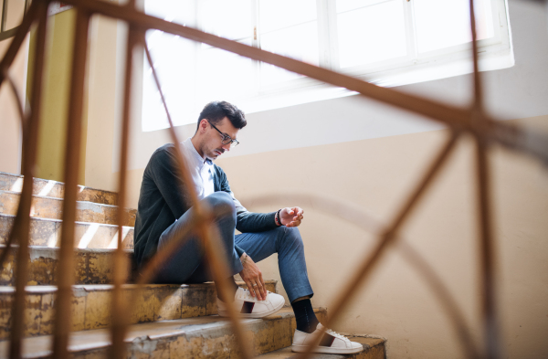 A handsome young man sitting indoors on staircase.