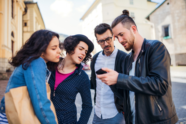 A group of young friends standing outdoor in town, using smartphone.