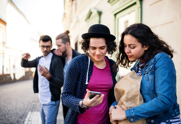 A group of young happy friends with smartphone standing outdoor in town, talking.