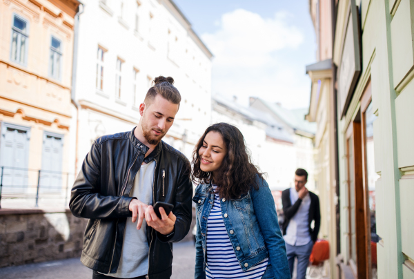 Young happy friends with a smartphone standing outdoor in town, talking.