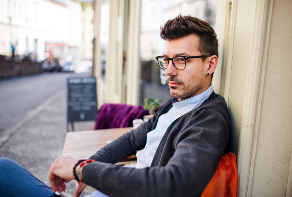 A portrait of young sad and serious man sitting in an outdoor cafe.