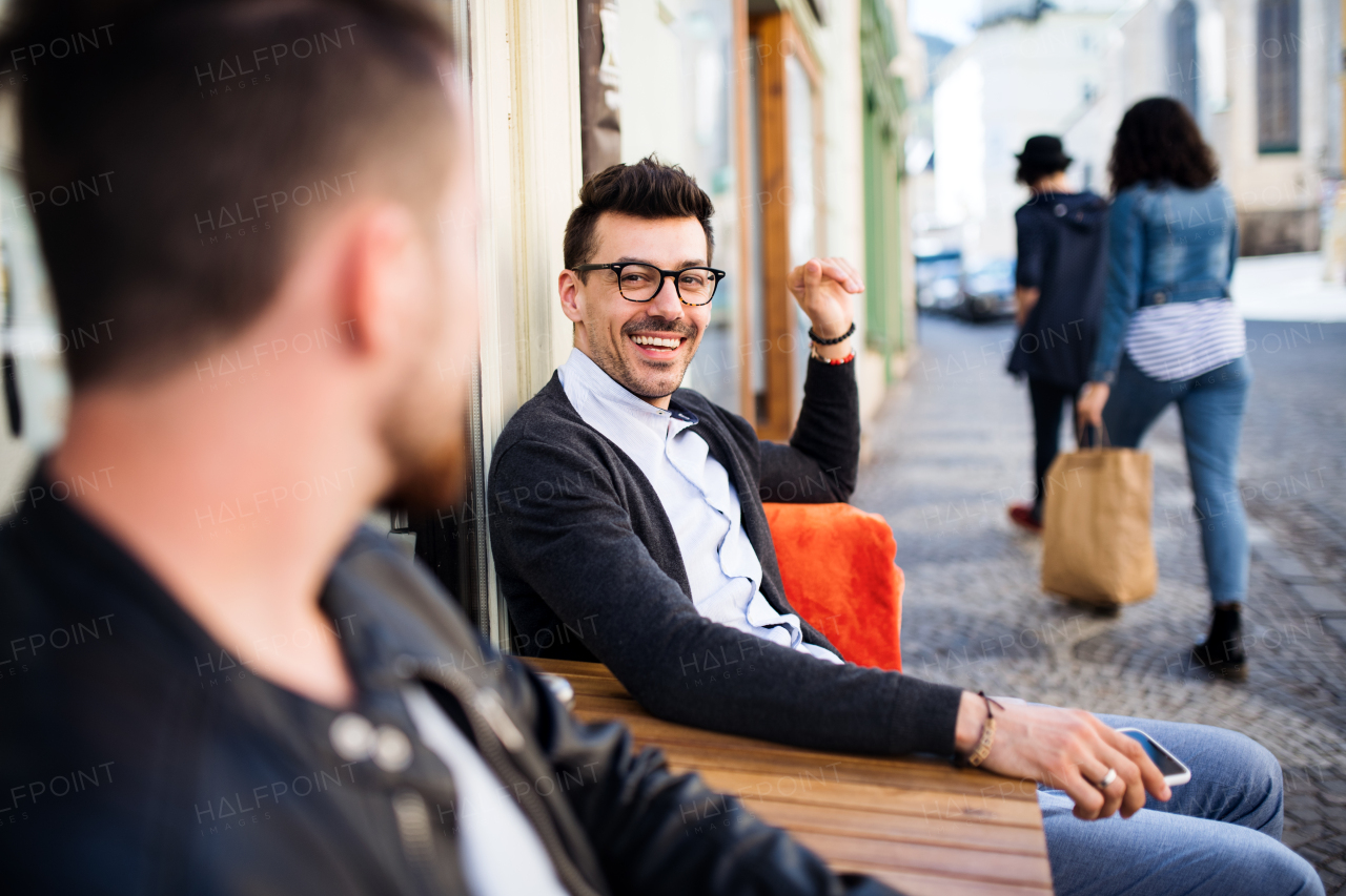 Young cheerful friends with smartphone sitting in an outdoor cafe, talking.