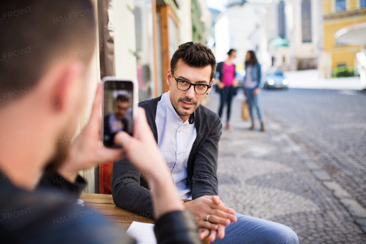 Young male friends with smartphone sitting in an outdoor cafe, taking a photograph.