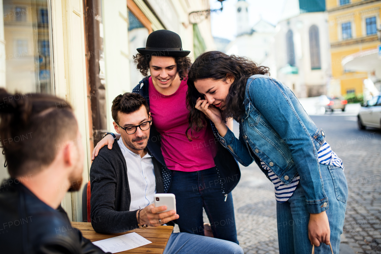 A group of young cheerful friends with smartphone sitting in an outdoor cafe, talking.