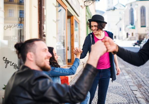 A group of young cheerful friends sitting in an outdoor cafe, greeting.