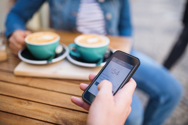 Midsection of unrecognizable young woman making online payment in outdoors cafe.