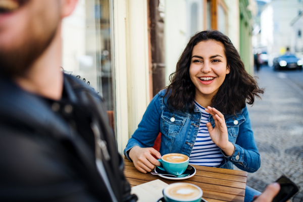 Young cheerful friends with coffee sitting in an outdoor cafe, talking.