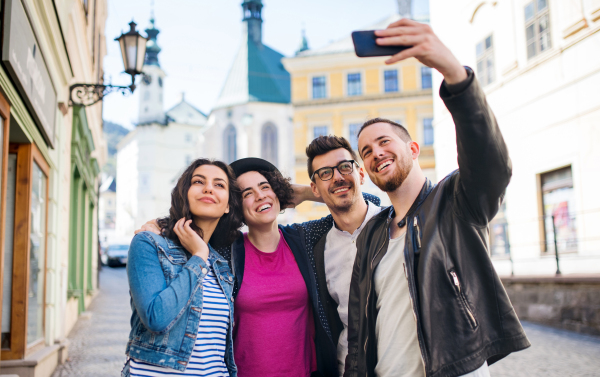 A group of young friends with smartphone standing outdoor in town, taking selfie.