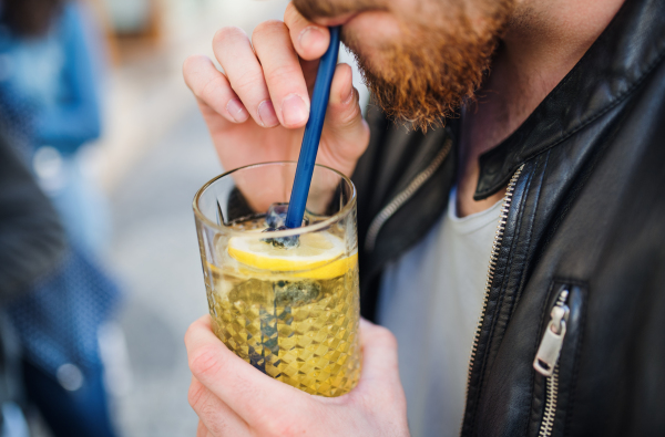 A midsection of bearded man in outdoor cafe, drinking lemonade with a straw.