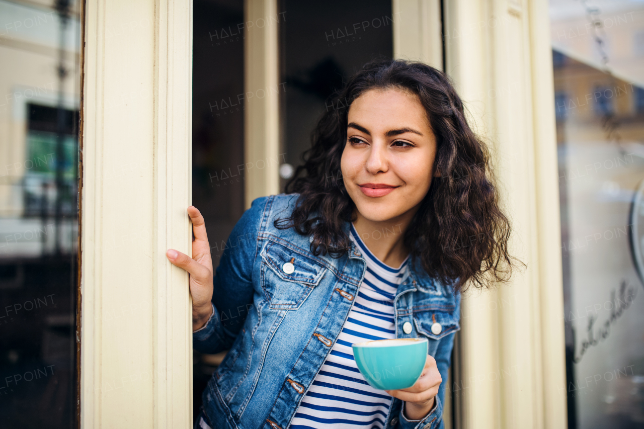 A beautiful young woman with tablet and coffee standing at the front door in cafe, waiting for somebody.