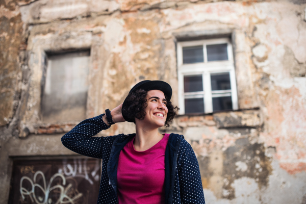 A young woman with hat standing outdoors in town, old building in the background.