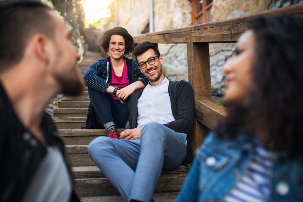 A portrait of group of young cheerful friends sitting outdoors on staircase in town.