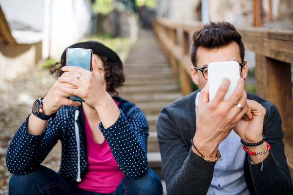 Young addicted friends sitting outdoors on staircase in town, using smartphone.