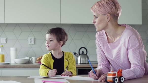 A young woman with small daughter drawing pictures in a kitchen.