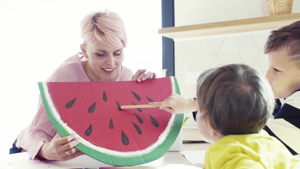 A happy young woman with two children drawing pictures in a kitchen.