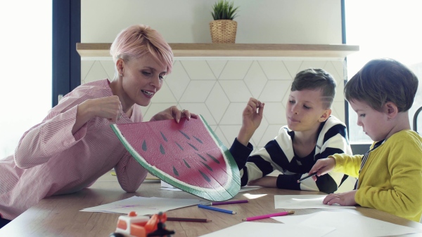 A happy young woman with two children drawing pictures in a kitchen.