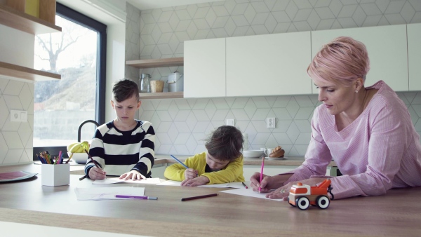 A happy young mother with two children drawing pictures in a kitchen.