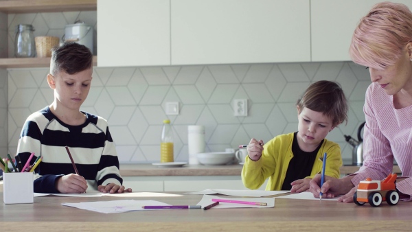 A happy young mother with two children drawing pictures in a kitchen.