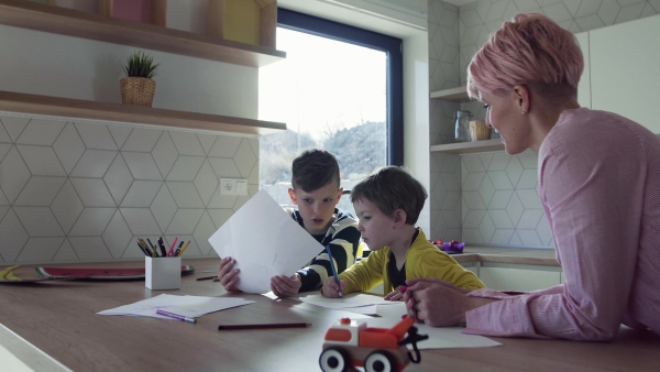 A happy young mother with two children drawing pictures in a kitchen.