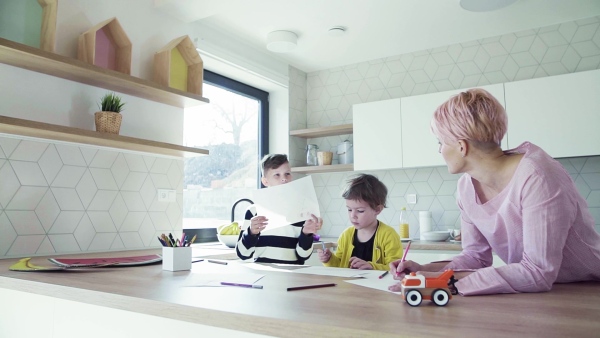 A happy young woman with two children drawing pictures in a kitchen. Slow motion.