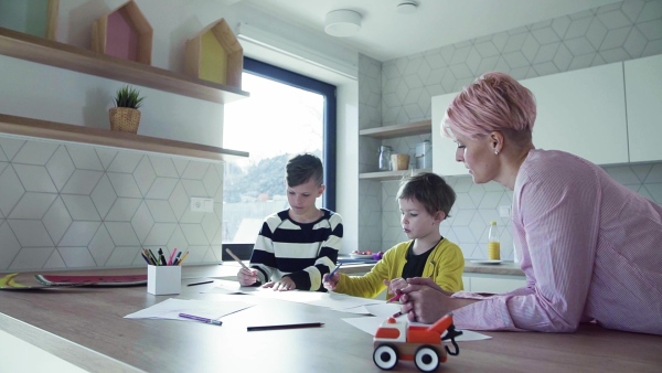 A happy young mother with two children drawing pictures in a kitchen. Slow motion.